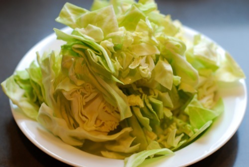 Half a cabbage is sliced thin and placed on a plate.