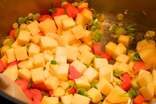 Turnips and carrots are added to a pan that already has green onions and garlic.