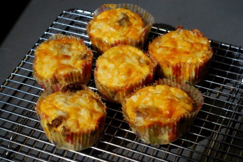 Six cooked frittata muffins with cheese and bacon cooling on a cooling rack.