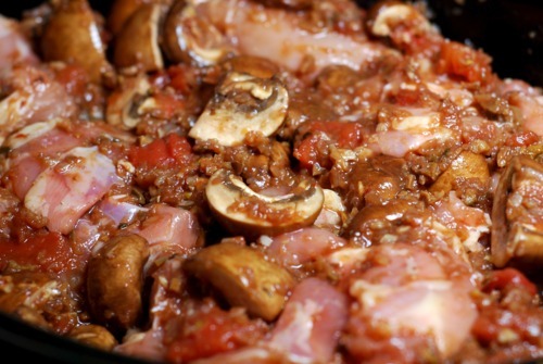 A slow cooker is filled with ingredients for a chicken cacciatore recipe. Shown is mushrooms and chicken.