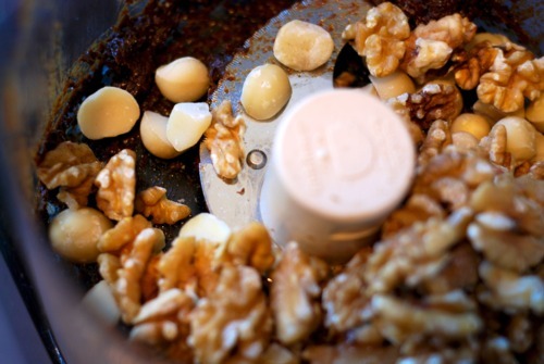 An overhead shot of an open food processor with pureed dates and whole walnuts and macadamia nuts.