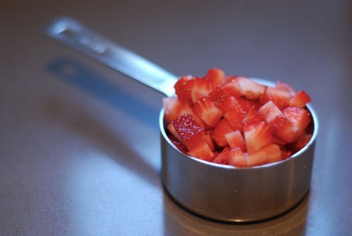 A silver measuring cup is filled with diced strawberries
