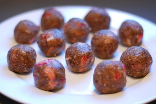 A round white plate is covered with strawberry energy bites that are rolled into balls.