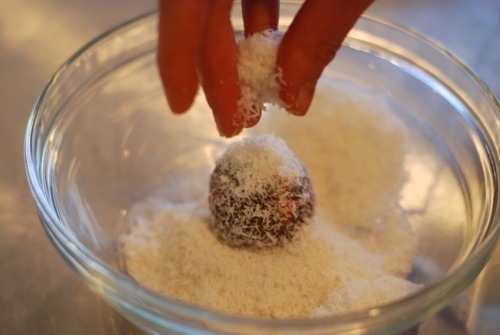A hand is sprinkling shredded coconut on top of a strawberry energy bite