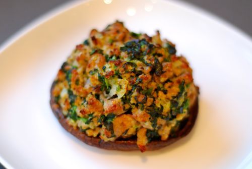 A browned sausage and spinach stuffed portobello mushroom on a plate.