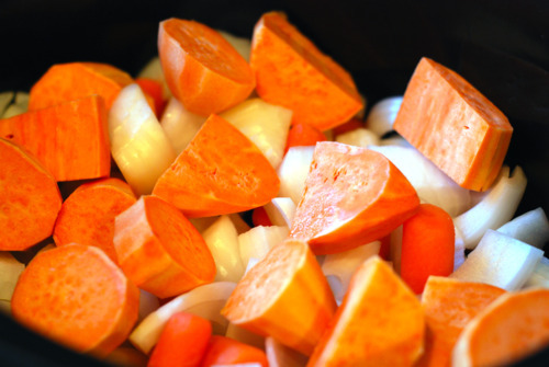 Chopped onions, carrots, and sweet potato in a slow cooker.