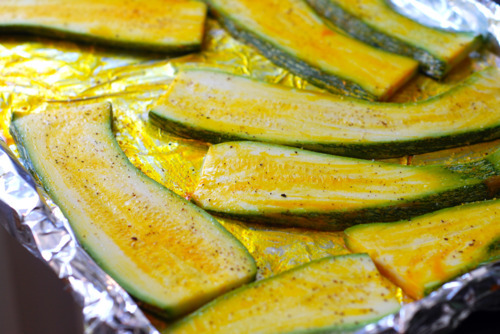 Sliced lengthwise pieces of zucchini are brushed with oil on a baking sheet.