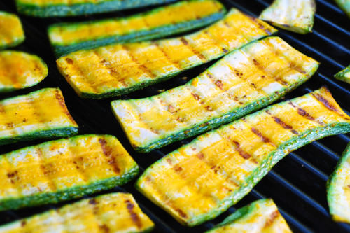 Slices of zucchini cooking on the grill with grill marks on top.