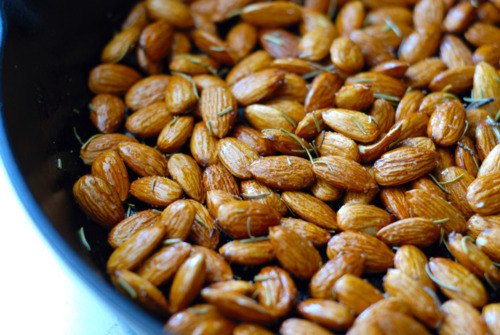 Almonds roasting on a pan with oil and dried rosemary.