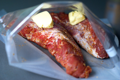 Two raw pork tenderloins in a sous vide bag with a pat of butter on top of each.