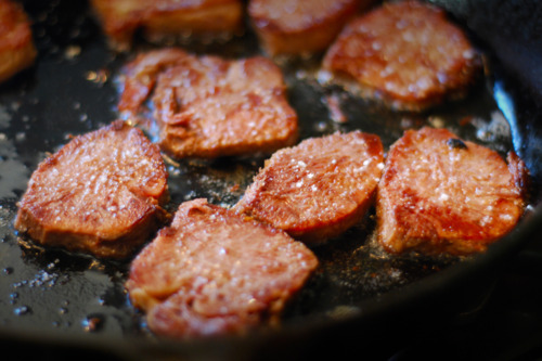 Slices of sous vide beef tongue frying in a cast iron pan.
