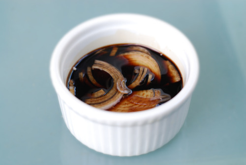 A small ramekin filled with sliced shallots and aged balsamic vinegar for Tomato Basil Salad.