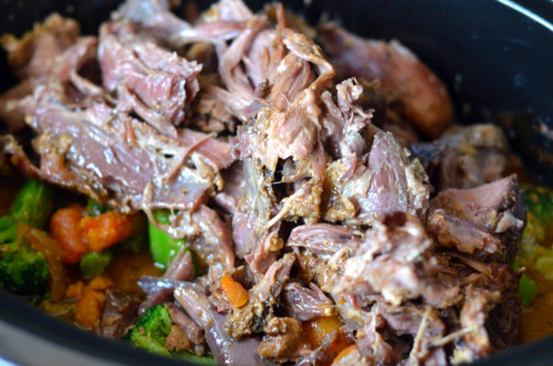 The shredded slow cooker curried goat meat is added back to the slow cooker.