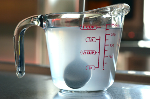 A salt water brine in a glass measuring cup with a spoon inside.