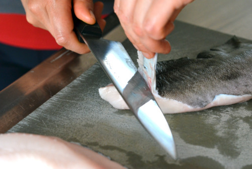 Someone cutting off the skin of a black cod fillet.