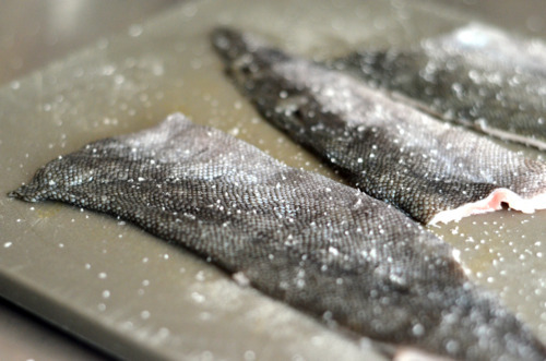 Black cod skins on a cutting board are generously salted.