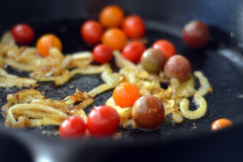 Sautéing onions and cherry tomatoes in a cast iron skillet.