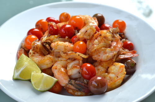 Sautéed Shrimp with Onions and Cherry Tomatoes on a plate with two lime wedges on the side.