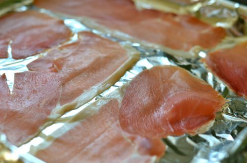 Slices of prosciutto laid out on a half sheet pan baking sheet.