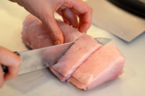 Someone cutting a tuna loin into 1.5 inch pieces.