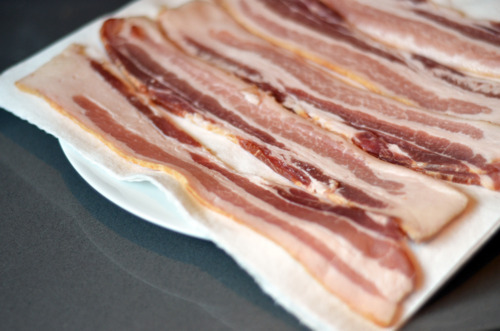 Slices of bacon lined up on a plate on top of paper towels.