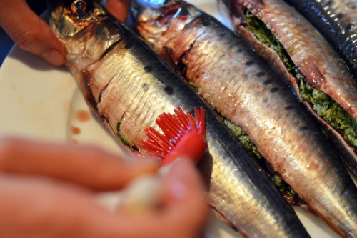 Someone brushing the skin of the sardines with bacon grease.