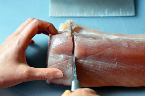 Someone cutting a raw albacore tuna crosswise into 1.5 inch chunks.