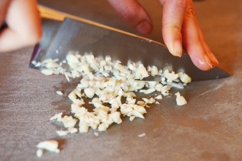 Someone chopping up garlic on a cutting board.