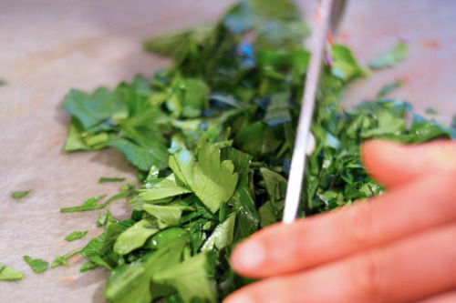 Someone chopping up parsley on a cutting board.