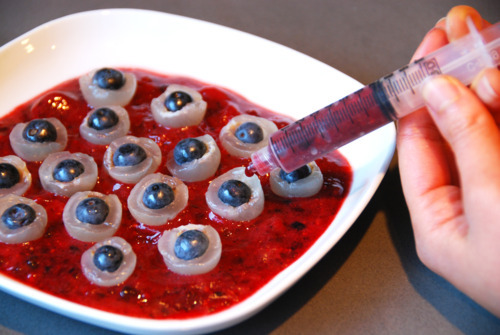 A bowl of blended frozen berries topped with the longan blueberry "eyeballs" with someone using a syringe to add the blended frozen berries on top of the "eyeballs."