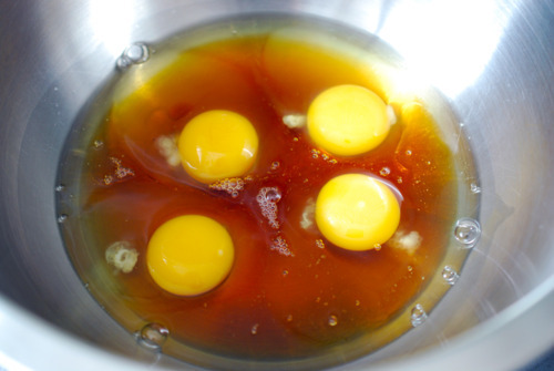 A silver bowl contains 4 large eggs and maple syrup.