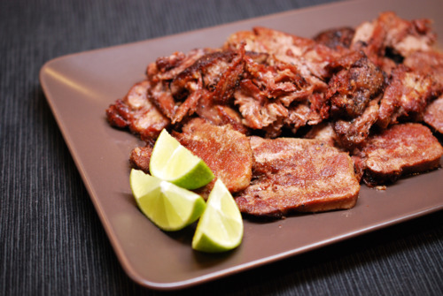 A plate of fried sous vide beef tongue with slices of lime on the side.