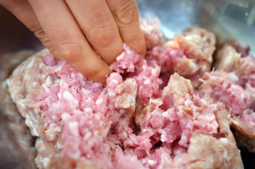Someone breaking up ground pork with their hands in a bowl.
