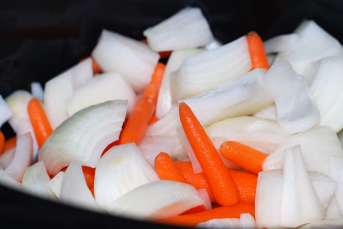 Chopped onions and baby carrots piled in a slow cooker.