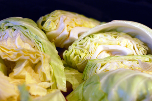 Wedges of green cabbage layered on top of onions and carrots in a slow cooker.