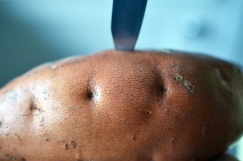 Someone stabbing through the skin of a sweet potato with a paring knife.