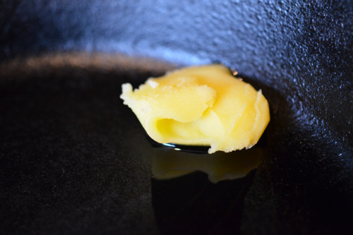 A spoonful of ghee melting in a cast iron skillet.