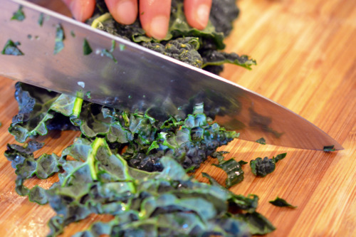 Someone chopping kale leaves with a knife on a cutting board.
