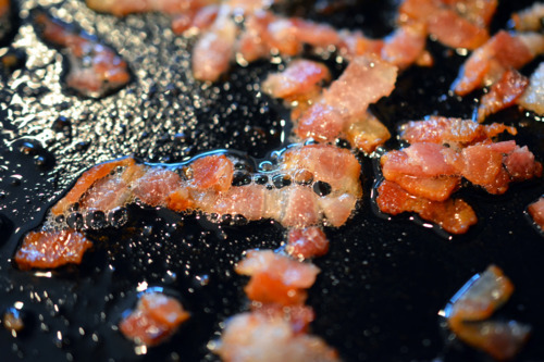 A close up of tiny pieces of bacon being fried in a cast iron skillet.