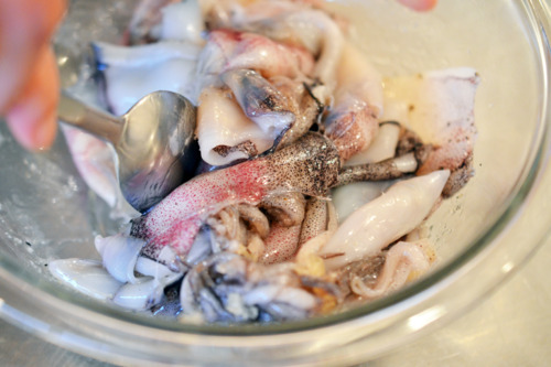 Tossing the raw squid with oil and seasoning in a bowl with a spoon.