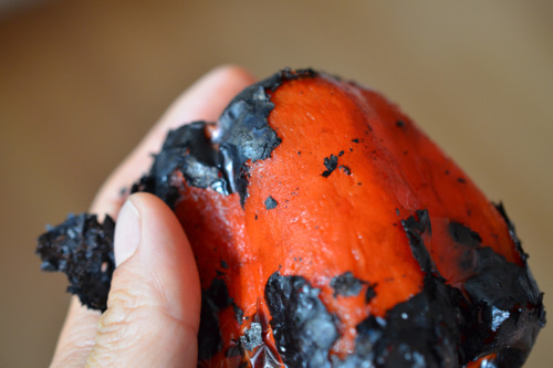 Someone rubbing off the blackened parts of a roasted red bell pepper.