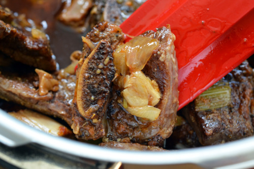 Porcini and Tomato Beef Short Ribs in a pressure cooker with the ingredients being stirred by a rubber spatula.