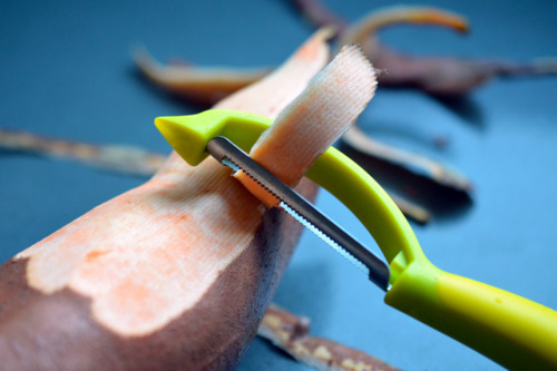 A close up of a sweet potato being peeled with a vegetable peeler.