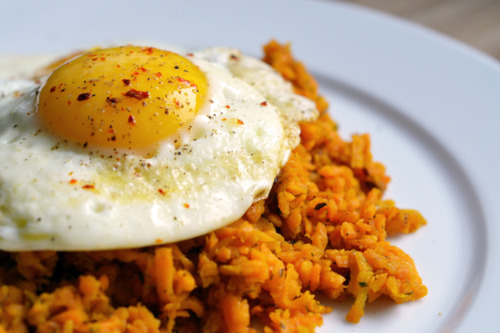 A side shot of Sweet Potato Hash with Fried Eggs on a white plate.