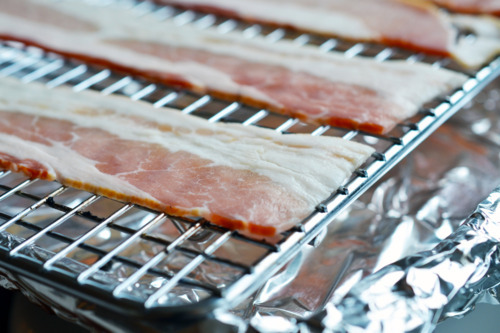 Raw bacon slices on a wire rack, ready to be cooked in the oven.