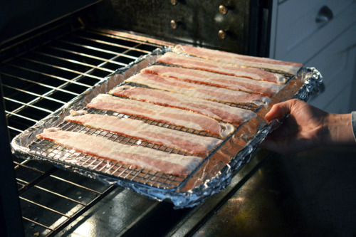 Someone putting in a tray of bacon to be baked in the oven.