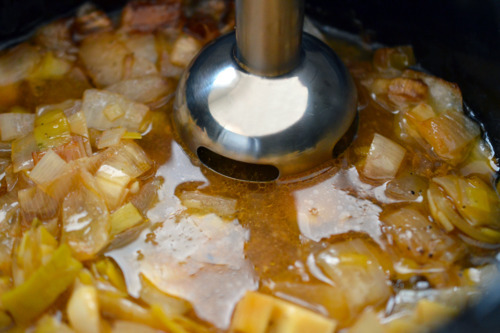 An immersion blender in a slow cooker is blending up the gravy.