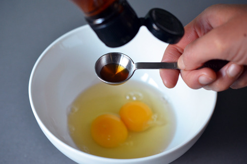 Measuring out fish sauce over a bowl with two cracked eggs.