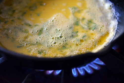 The scrambled egg mixture is added into the cast iron pan, cooking in a thin layer.