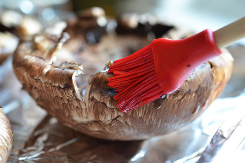 A portobello mushroom is brushed with oil with a silicone brush.